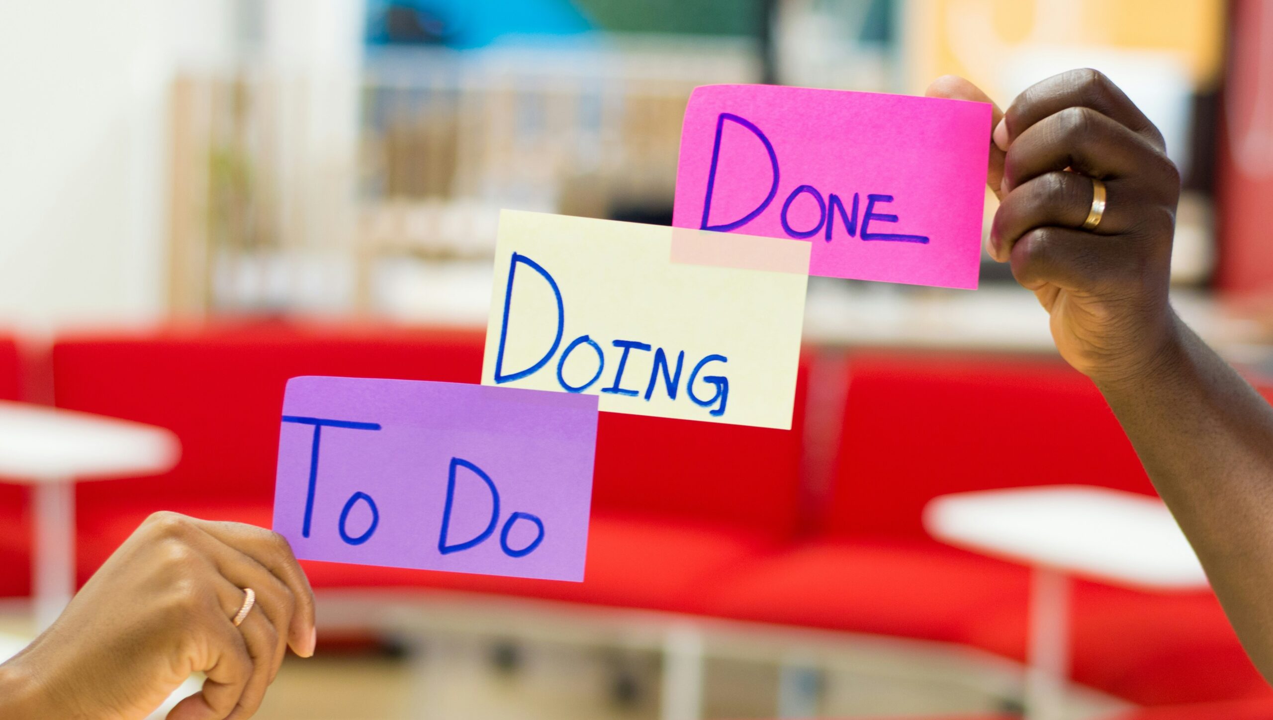 Hands sticking three colored post its to a window with the the labels To Do, Doing, and Done.