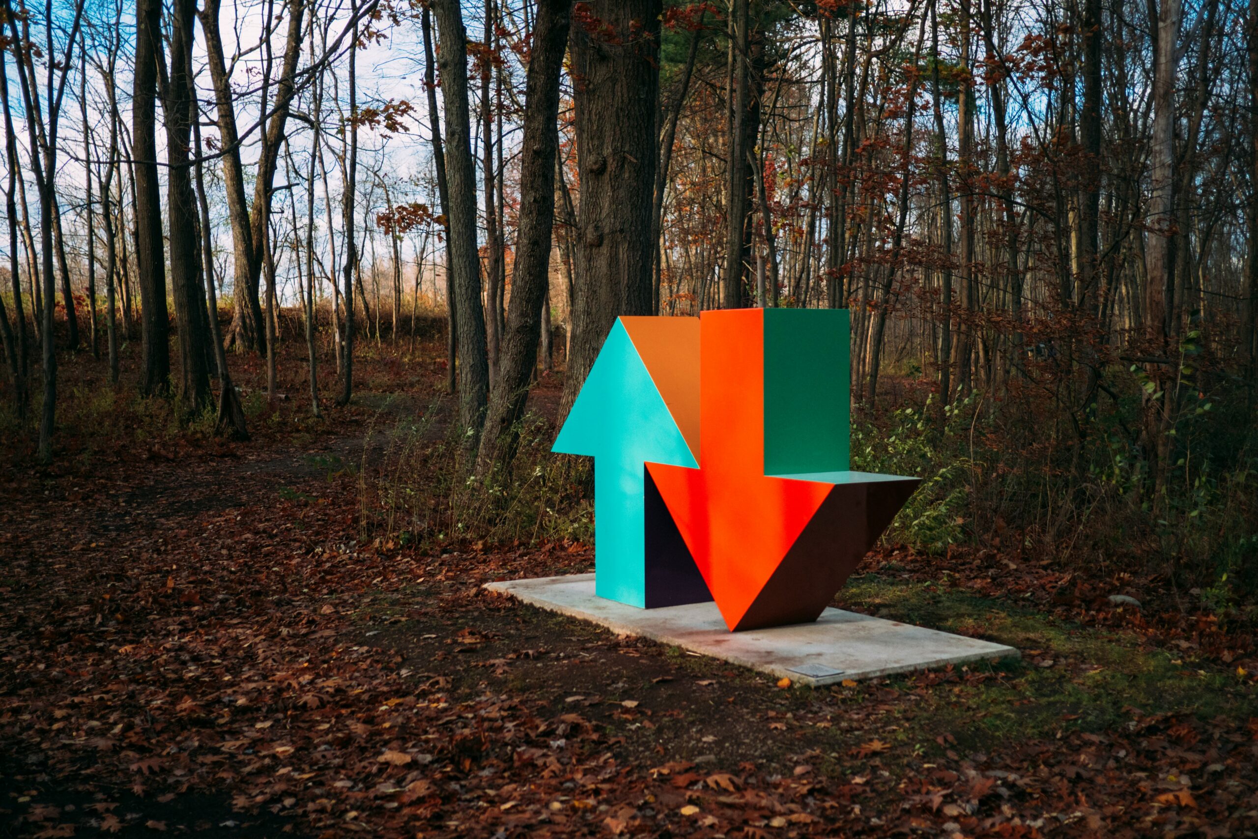 Sculpture of blue up arrow and red down arrow in forrest setting.