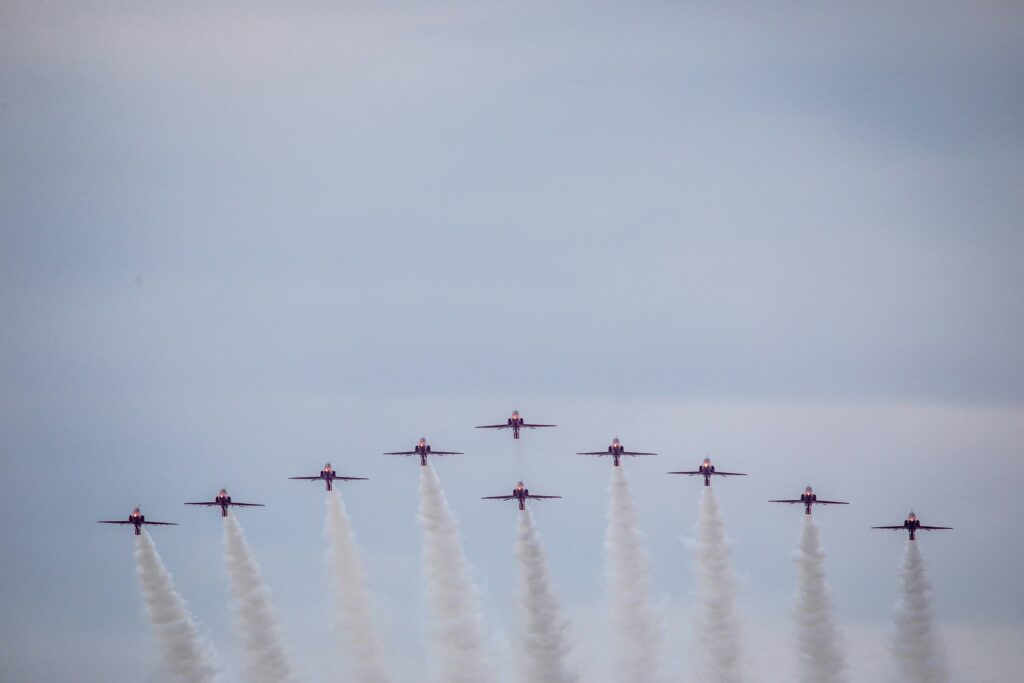 Ten military planes flying in tandem with streams flowing behind them.
