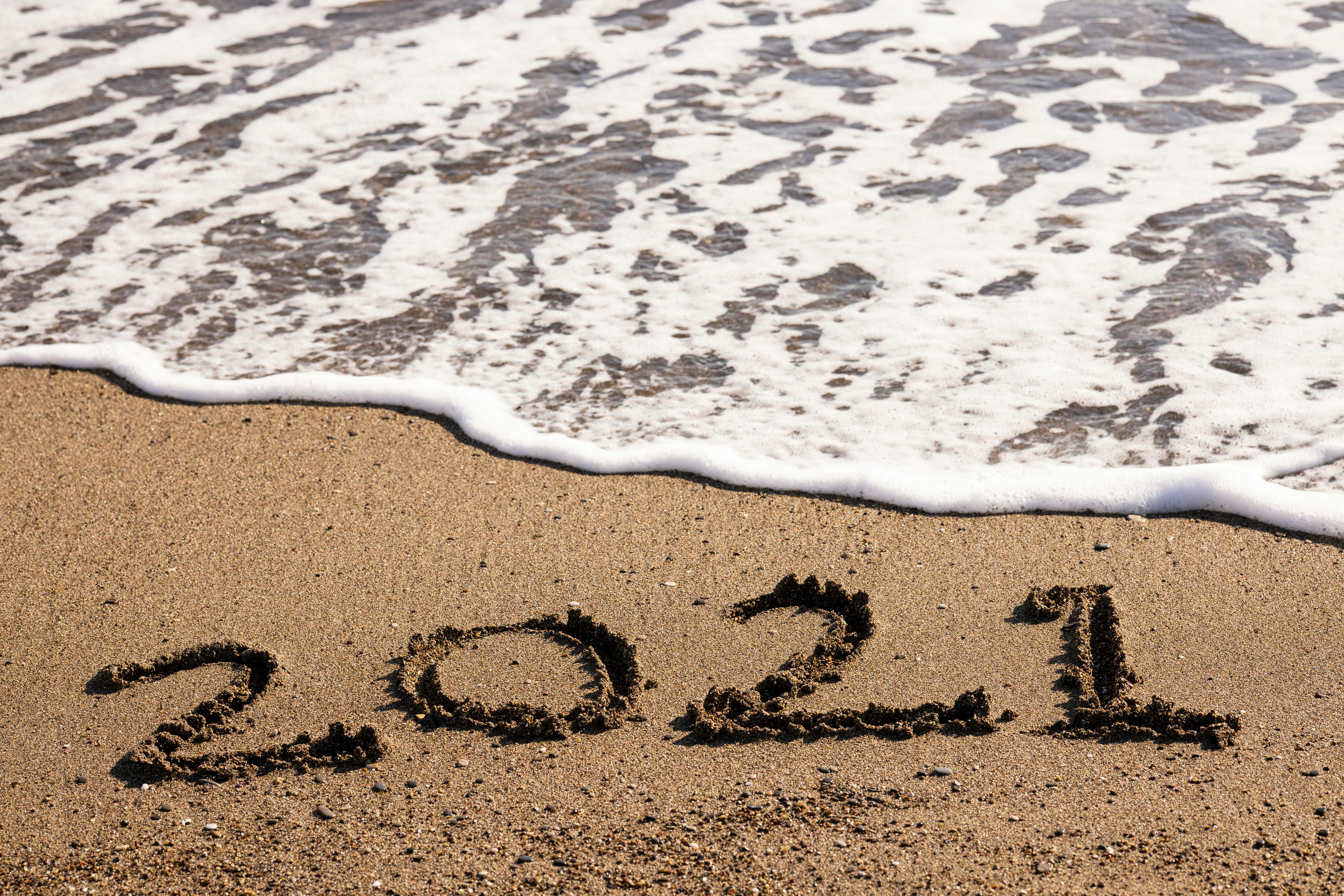 2021 in sand on beach with tide coming in behind it.