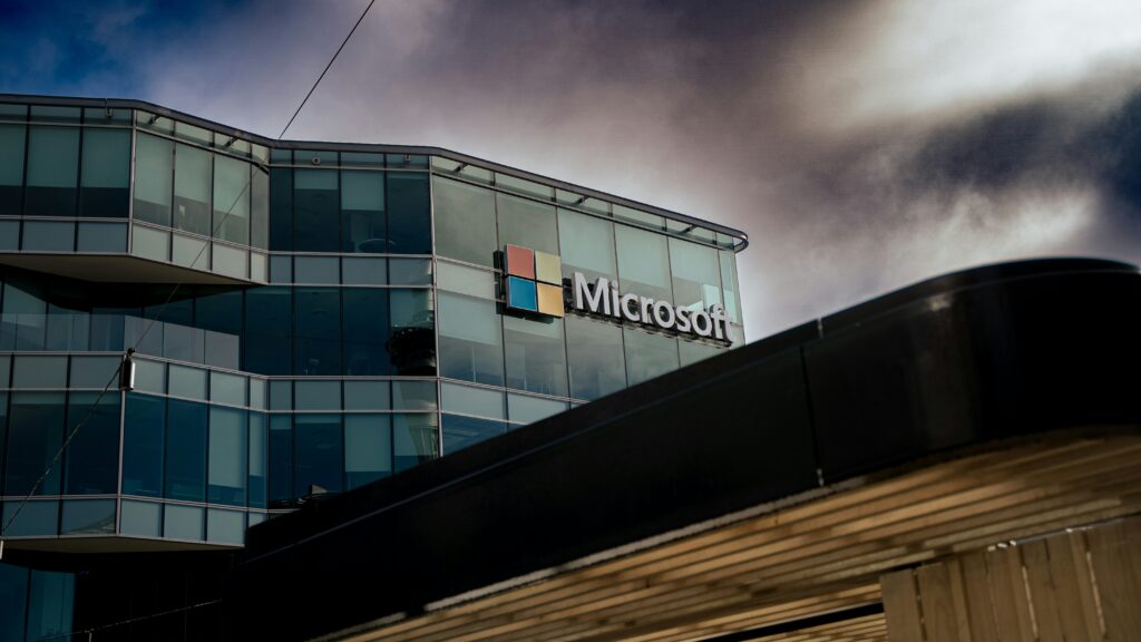       A modern Microsoft office building with large glass windows and the Microsoft logo on the facade, set against a dramatic cloudy sky.